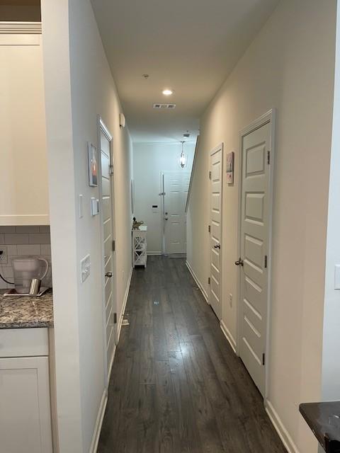 hallway with dark wood finished floors, visible vents, and baseboards