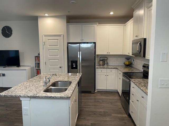 kitchen with light stone counters, stainless steel appliances, white cabinets, a kitchen island with sink, and a sink