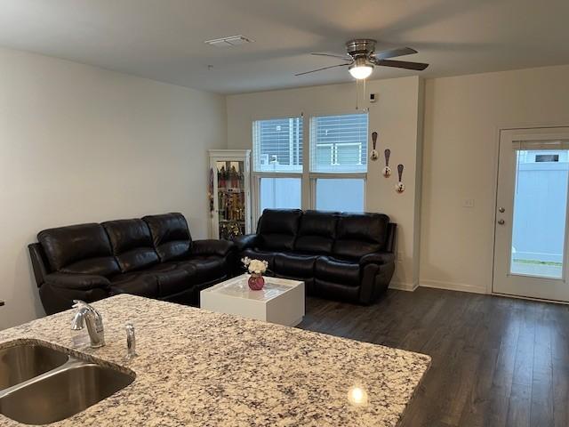 living area featuring a ceiling fan, visible vents, and dark wood finished floors