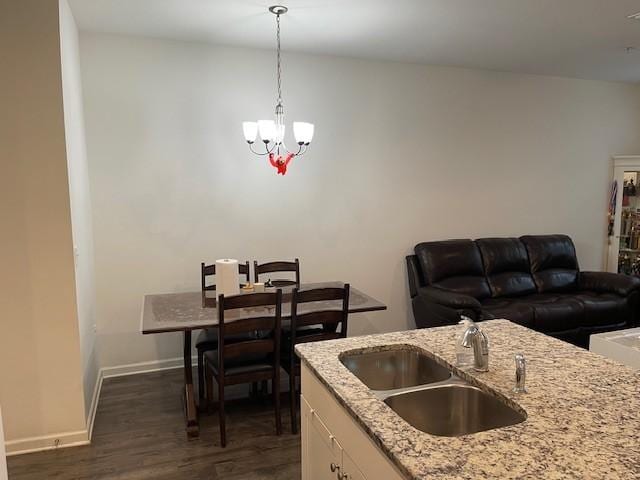 kitchen with white cabinets, light stone counters, dark wood-style flooring, hanging light fixtures, and a sink