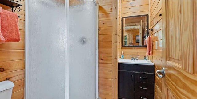 bathroom featuring vanity, a shower with shower door, wooden walls, and toilet