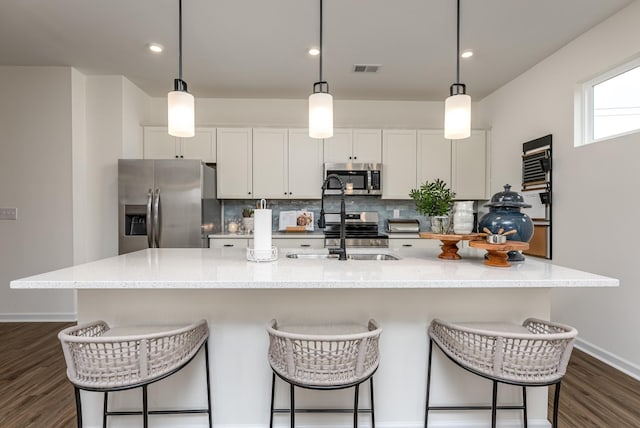 kitchen featuring stainless steel appliances, tasteful backsplash, a center island with sink, and decorative light fixtures