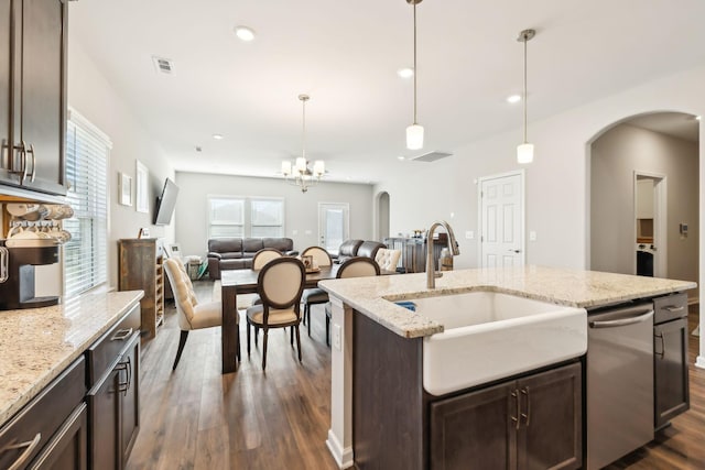 kitchen featuring decorative light fixtures, sink, a kitchen island with sink, dark brown cabinetry, and light stone countertops