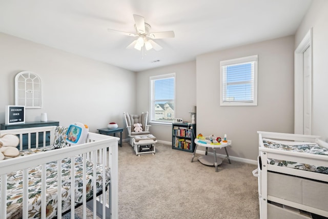 bedroom featuring a nursery area, ceiling fan, and light colored carpet