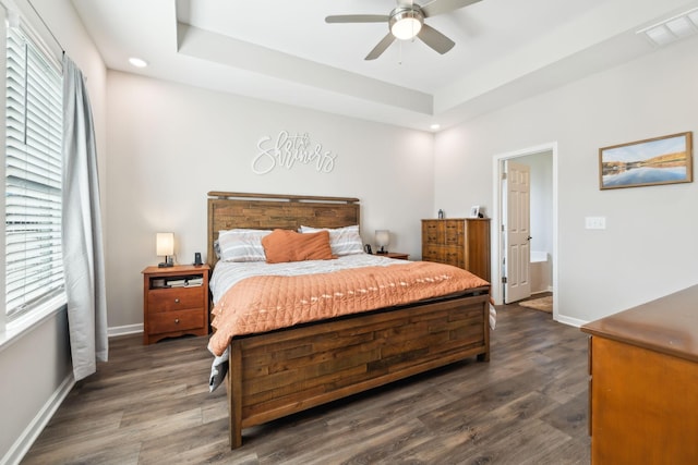 bedroom featuring dark hardwood / wood-style floors, ceiling fan, a tray ceiling, and ensuite bath