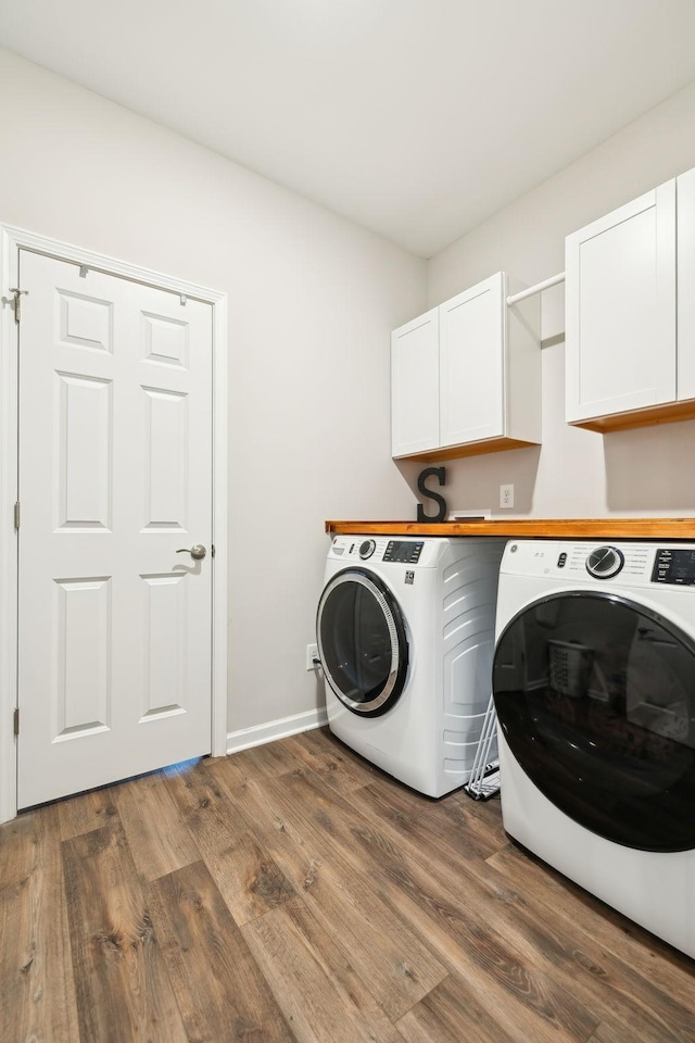 clothes washing area with washer and dryer, dark wood-type flooring, and cabinets