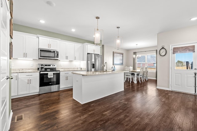 kitchen with stainless steel appliances, a center island with sink, pendant lighting, and white cabinets