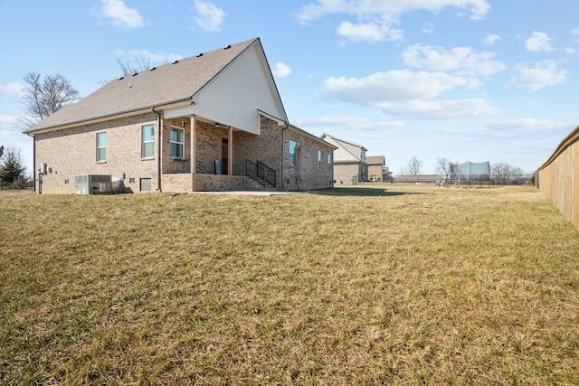 rear view of property with a yard, central AC, and a trampoline