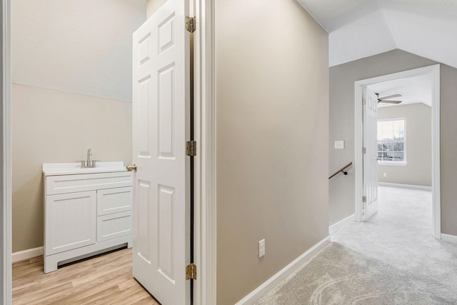 corridor with lofted ceiling, sink, and light carpet