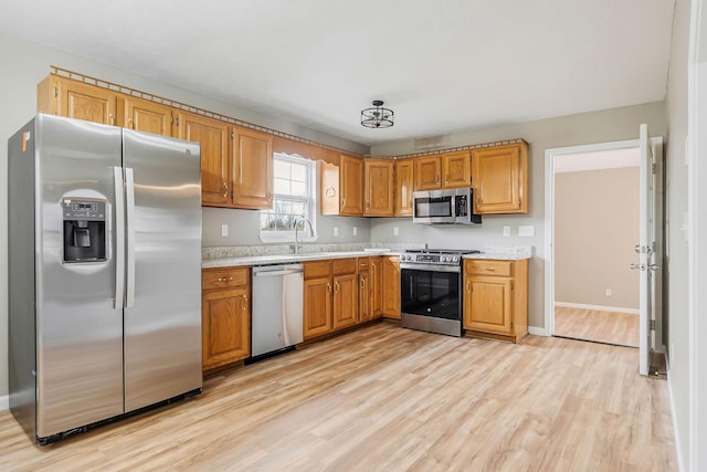 kitchen with appliances with stainless steel finishes, sink, and light hardwood / wood-style flooring