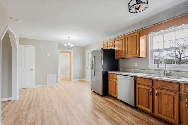 kitchen featuring sink, an inviting chandelier, stainless steel appliances, decorative light fixtures, and light wood-type flooring