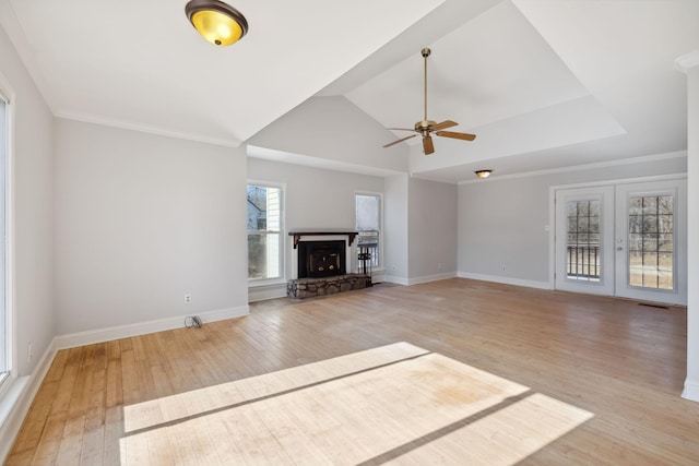 unfurnished living room with crown molding, light hardwood / wood-style flooring, ceiling fan, a stone fireplace, and french doors