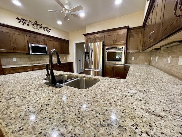 kitchen with sink, backsplash, light stone countertops, and appliances with stainless steel finishes