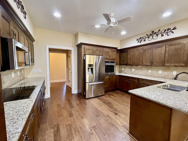 kitchen featuring appliances with stainless steel finishes, wood-type flooring, sink, decorative backsplash, and light stone countertops