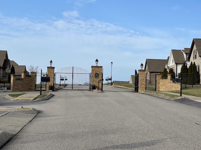 view of street featuring a gate, sidewalks, curbs, street lights, and a gated entry