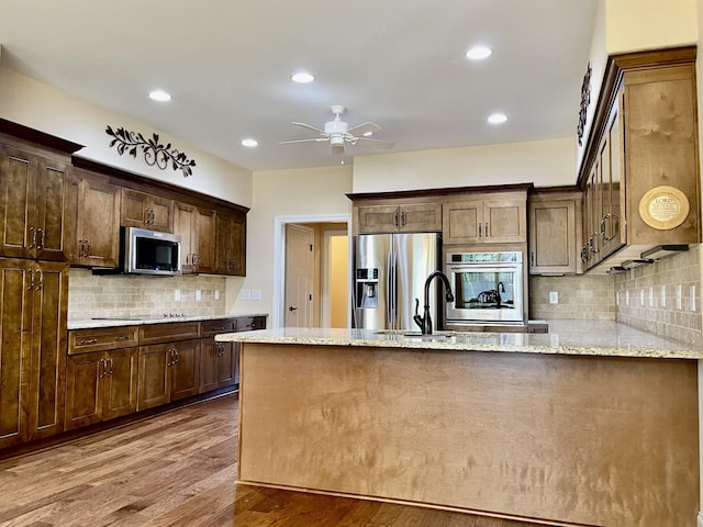 kitchen with a ceiling fan, wood finished floors, a peninsula, appliances with stainless steel finishes, and light stone countertops