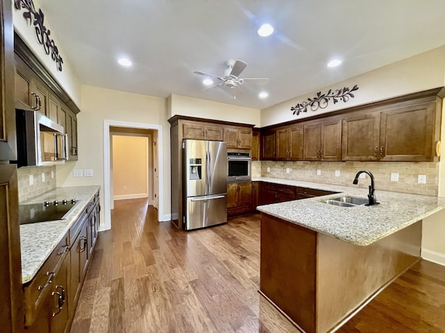 kitchen featuring light stone countertops, a peninsula, a sink, dark wood-type flooring, and appliances with stainless steel finishes