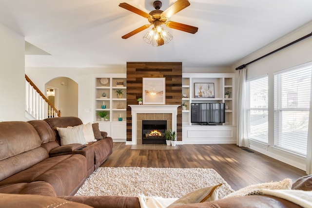 living room with dark hardwood / wood-style floors, ceiling fan, a fireplace, and built in shelves