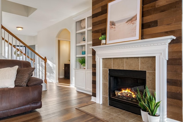 living room featuring wood-type flooring, a tile fireplace, and built in features