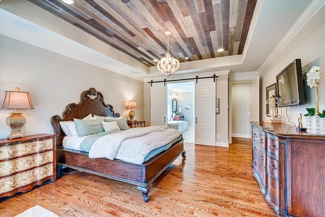 bedroom featuring connected bathroom, a tray ceiling, light hardwood / wood-style floors, ornamental molding, and a barn door