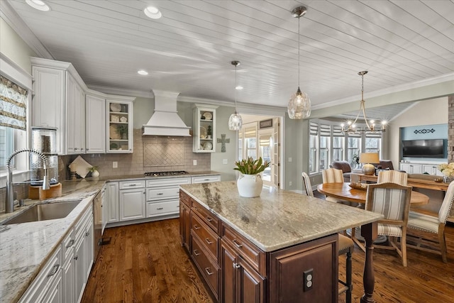 kitchen featuring sink, custom exhaust hood, light stone counters, a center island, and white cabinets