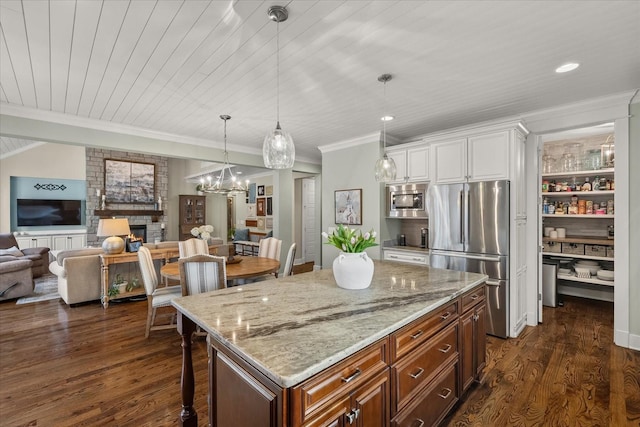 kitchen with appliances with stainless steel finishes, hanging light fixtures, dark hardwood / wood-style floors, a large fireplace, and a kitchen island