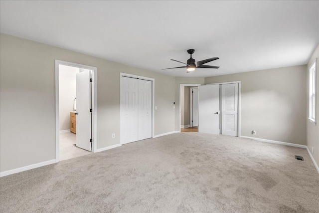 unfurnished bedroom featuring two closets, connected bathroom, light colored carpet, and ceiling fan