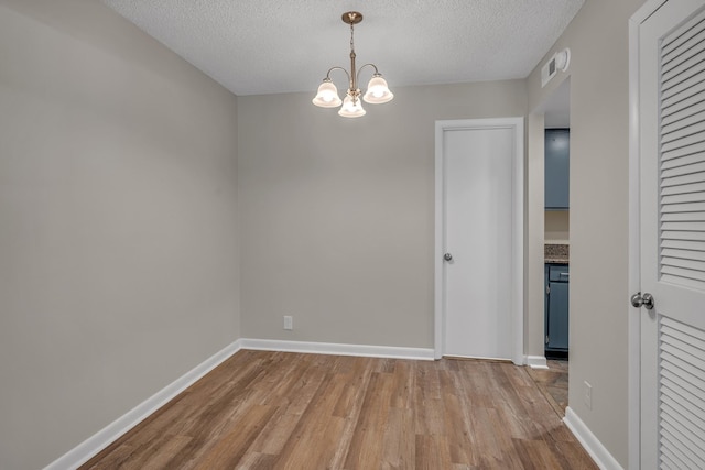 spare room with a chandelier, a textured ceiling, and light wood-type flooring