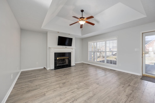 unfurnished living room featuring a tiled fireplace, ceiling fan, a raised ceiling, and light wood-type flooring