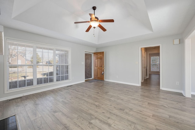 unfurnished living room with plenty of natural light, a tray ceiling, and light hardwood / wood-style floors