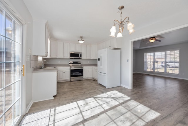 kitchen with appliances with stainless steel finishes, sink, white cabinets, hanging light fixtures, and light hardwood / wood-style floors