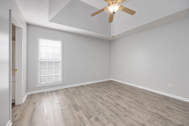 spare room with ceiling fan, a tray ceiling, and light wood-type flooring