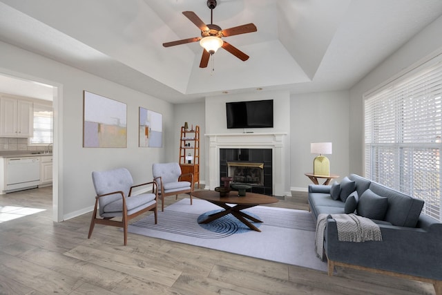 living room featuring ceiling fan, a fireplace, a tray ceiling, and light wood-type flooring