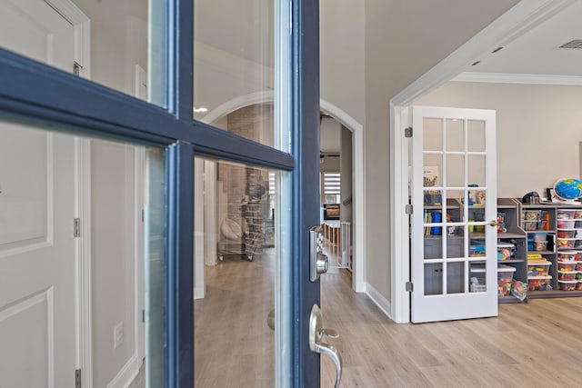 doorway with ornamental molding and light hardwood / wood-style floors