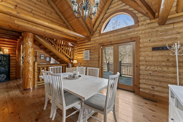 dining area with hardwood / wood-style floors, log walls, and high vaulted ceiling