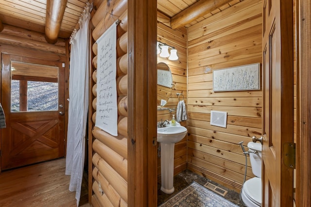 bathroom with wood ceiling, beam ceiling, rustic walls, and toilet