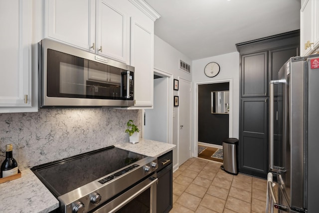 kitchen with light tile patterned flooring, white cabinetry, stainless steel appliances, light stone countertops, and decorative backsplash