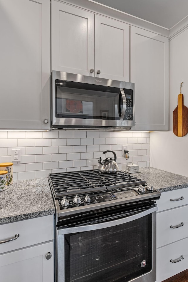 kitchen with ornamental molding, appliances with stainless steel finishes, white cabinets, and light stone counters