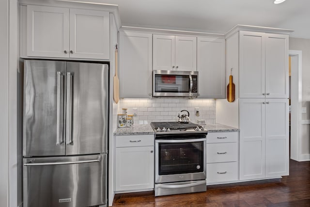 kitchen featuring appliances with stainless steel finishes, white cabinetry, backsplash, dark hardwood / wood-style floors, and light stone counters