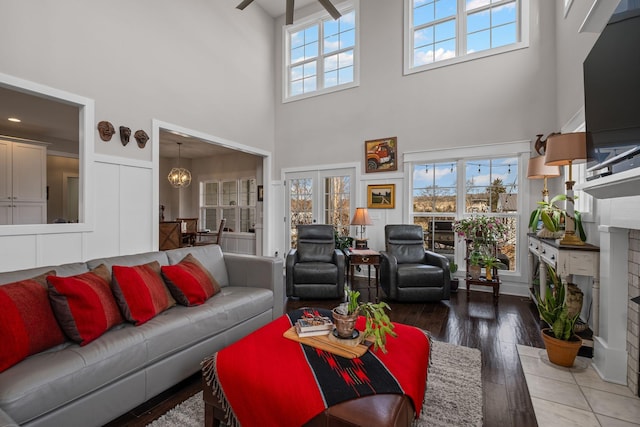 living room with french doors, a towering ceiling, wood-type flooring, and ceiling fan with notable chandelier