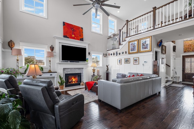 living room featuring ceiling fan, dark hardwood / wood-style flooring, a tile fireplace, and a high ceiling