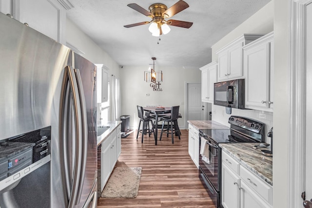 kitchen featuring tasteful backsplash, light stone countertops, black appliances, white cabinets, and decorative light fixtures