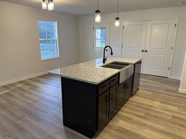 kitchen featuring pendant lighting, sink, a kitchen island with sink, stainless steel dishwasher, and light stone countertops