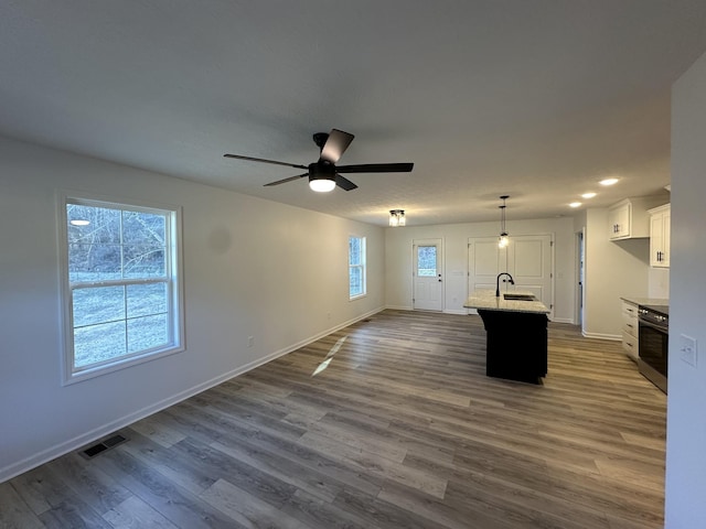 kitchen featuring dark hardwood / wood-style floors, sink, stainless steel range with electric cooktop, white cabinets, and a center island with sink