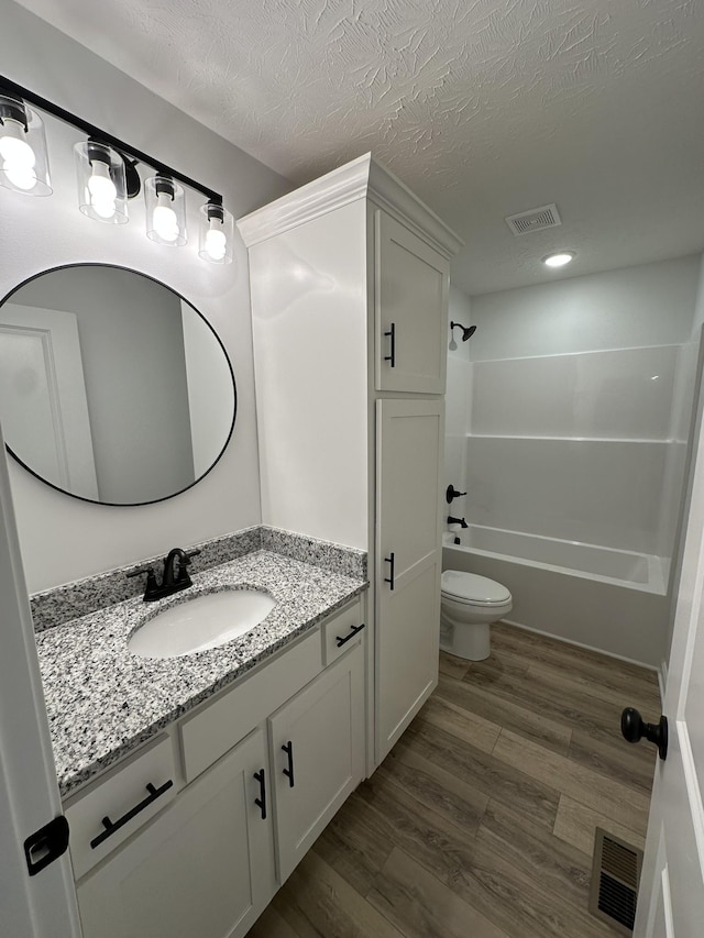 full bathroom featuring hardwood / wood-style flooring,  shower combination, vanity, a textured ceiling, and toilet