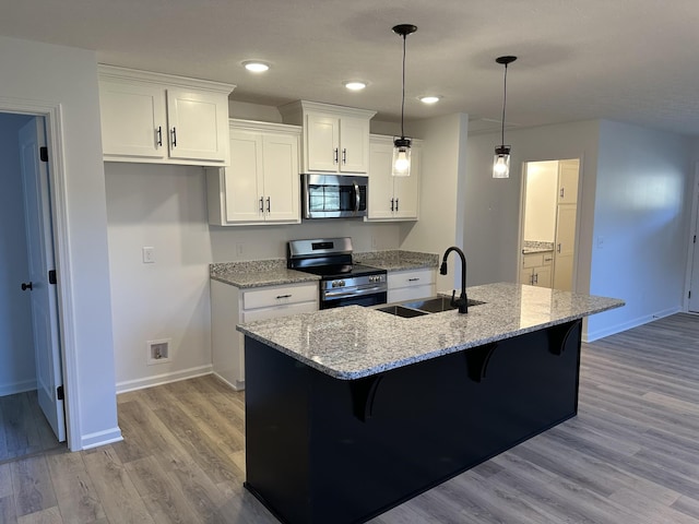 kitchen with sink, light stone counters, appliances with stainless steel finishes, an island with sink, and white cabinets