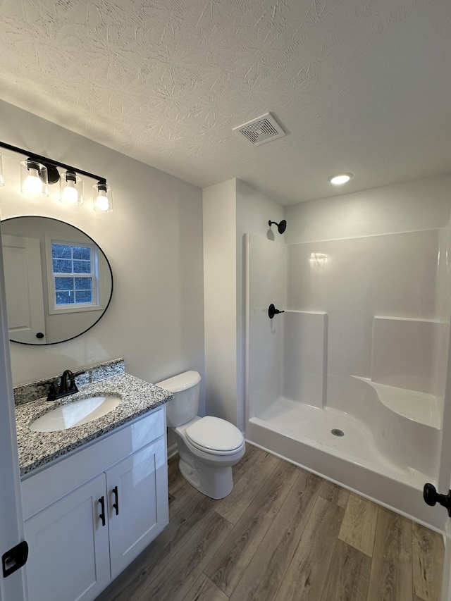 bathroom featuring wood-type flooring, vanity, walk in shower, toilet, and a textured ceiling