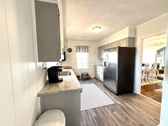 kitchen featuring dark wood-style flooring, light stone countertops, stainless steel appliances, a textured ceiling, and a notable chandelier