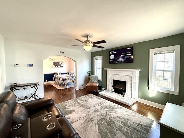 living area with dark wood-type flooring, plenty of natural light, a fireplace, and a ceiling fan