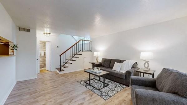 living area featuring stairway, baseboards, visible vents, and wood finished floors